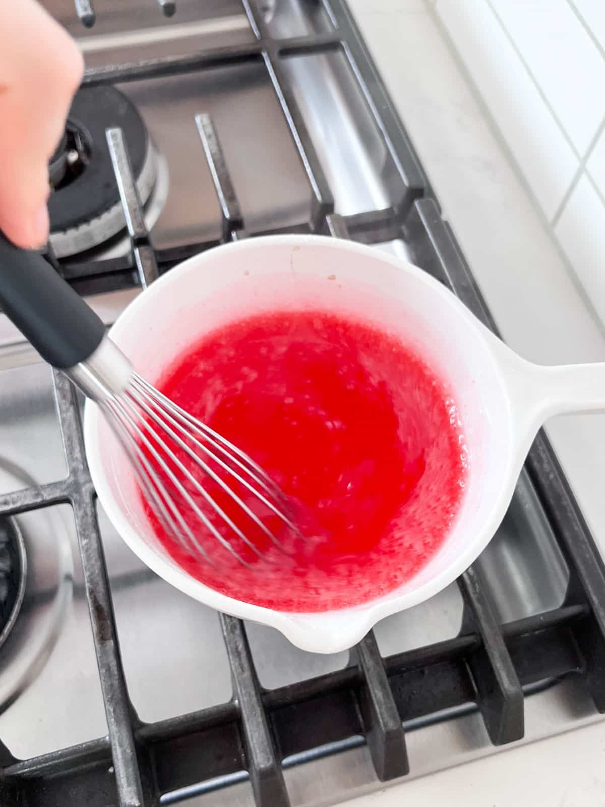 Jello mix being whisked into the thickened glaze off the heat.