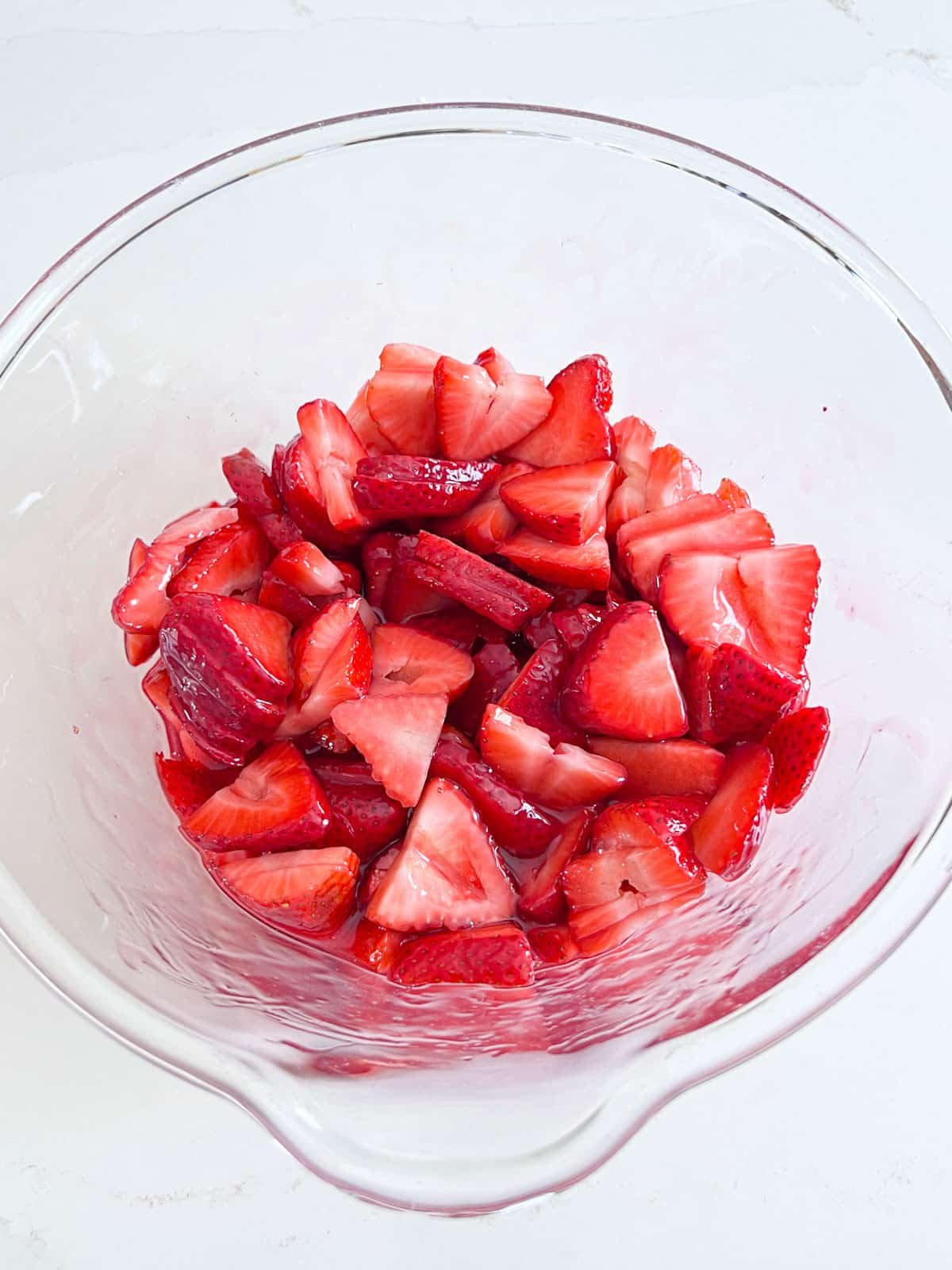 Sliced strawberries in a glass bowl with the hot glaze poured over the top of it.