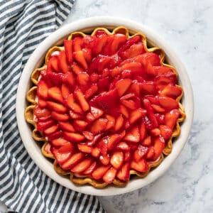 An overhead image of a strawberry cream pie with a striped napkin next to it.