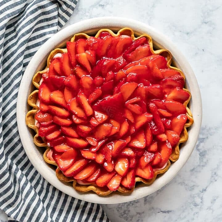 An overhead image of a strawberry cream pie with a striped napkin next to it.
