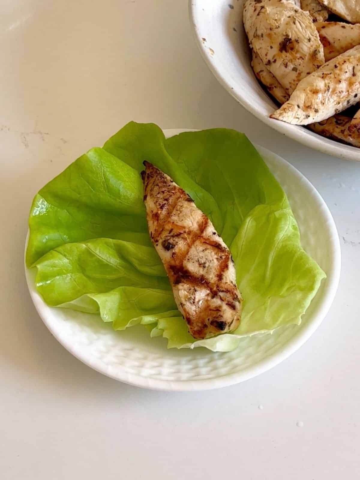 Chicken on a lettuce wrap on a white plate.