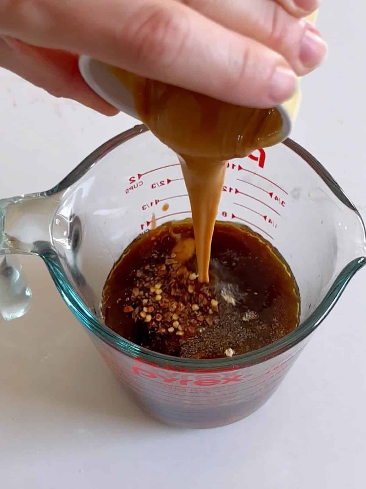 Peanut sauce ingredients in a large measuring cup with peanut butter being poured in.