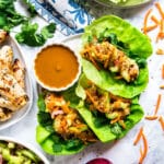 An overhead image of a plate of chicken lettuce wraps with peanut sauce next to it and all the fixings surrounding it.