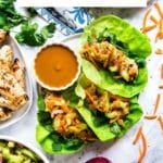 An overhead image of a plate of chicken lettuce wraps with peanut sauce next to it and all the fixings surrounding it.