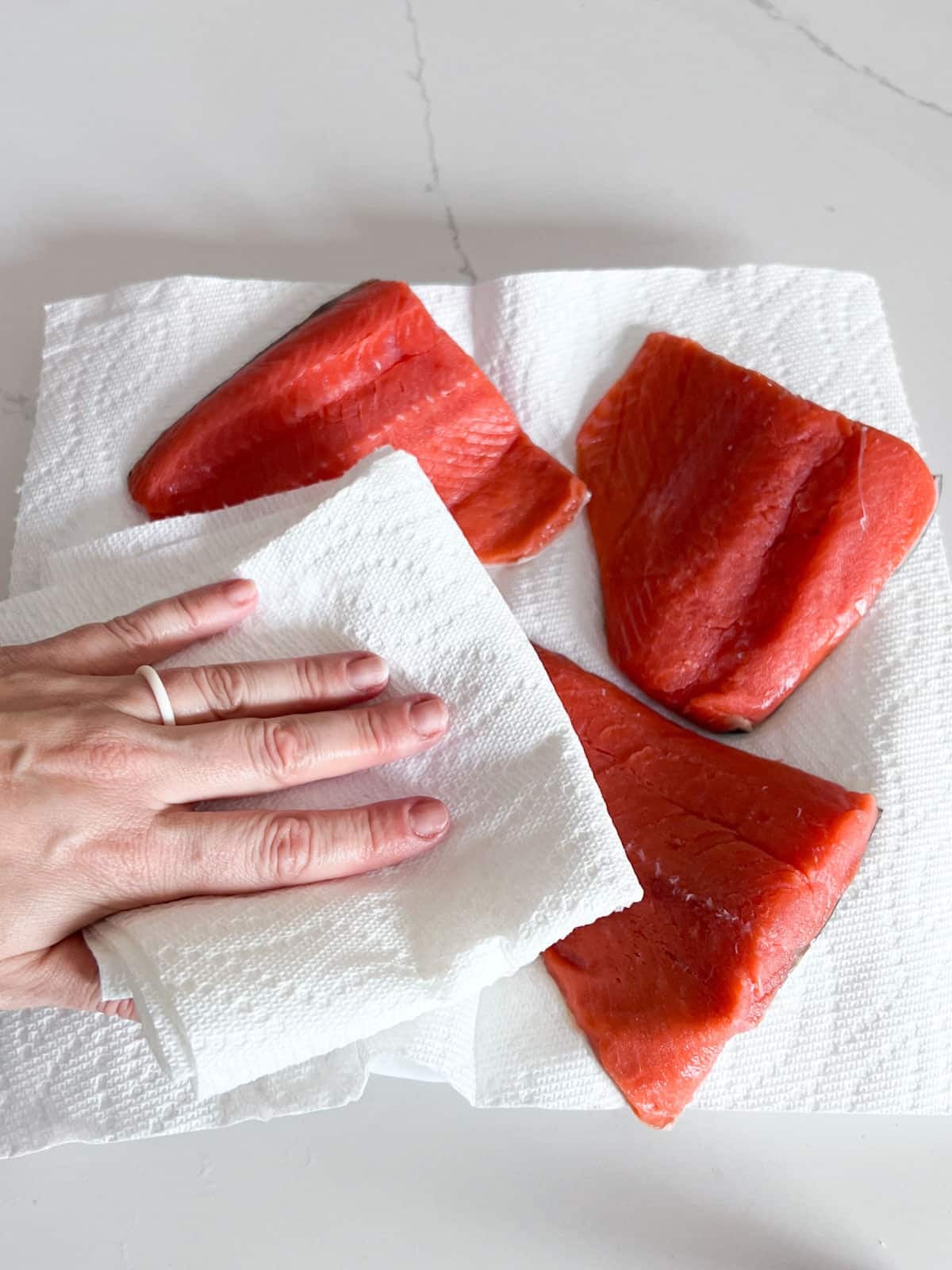 A hand patting salmon filets with paper towel.