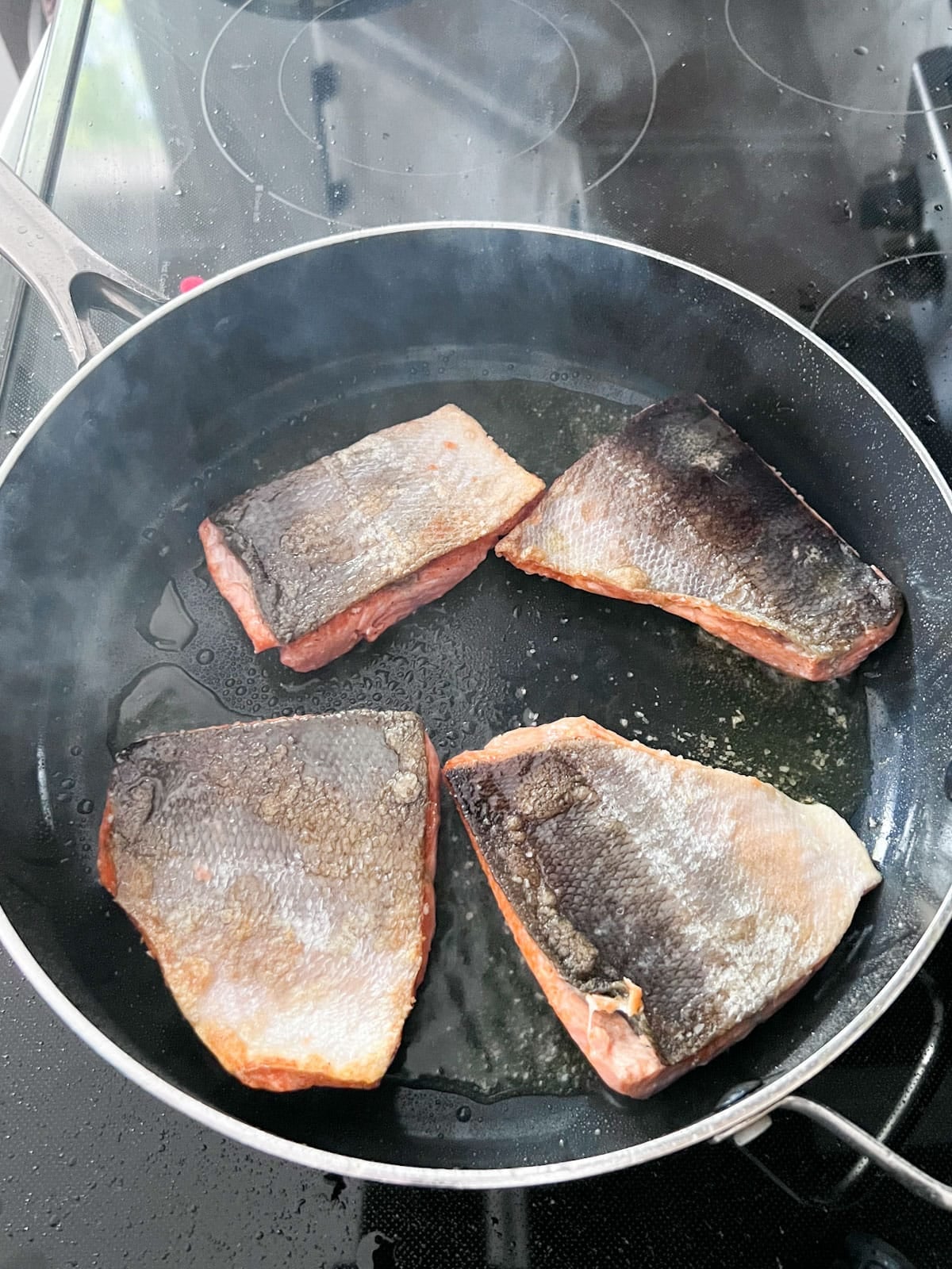 Salmon searing with skin side up after being turned.