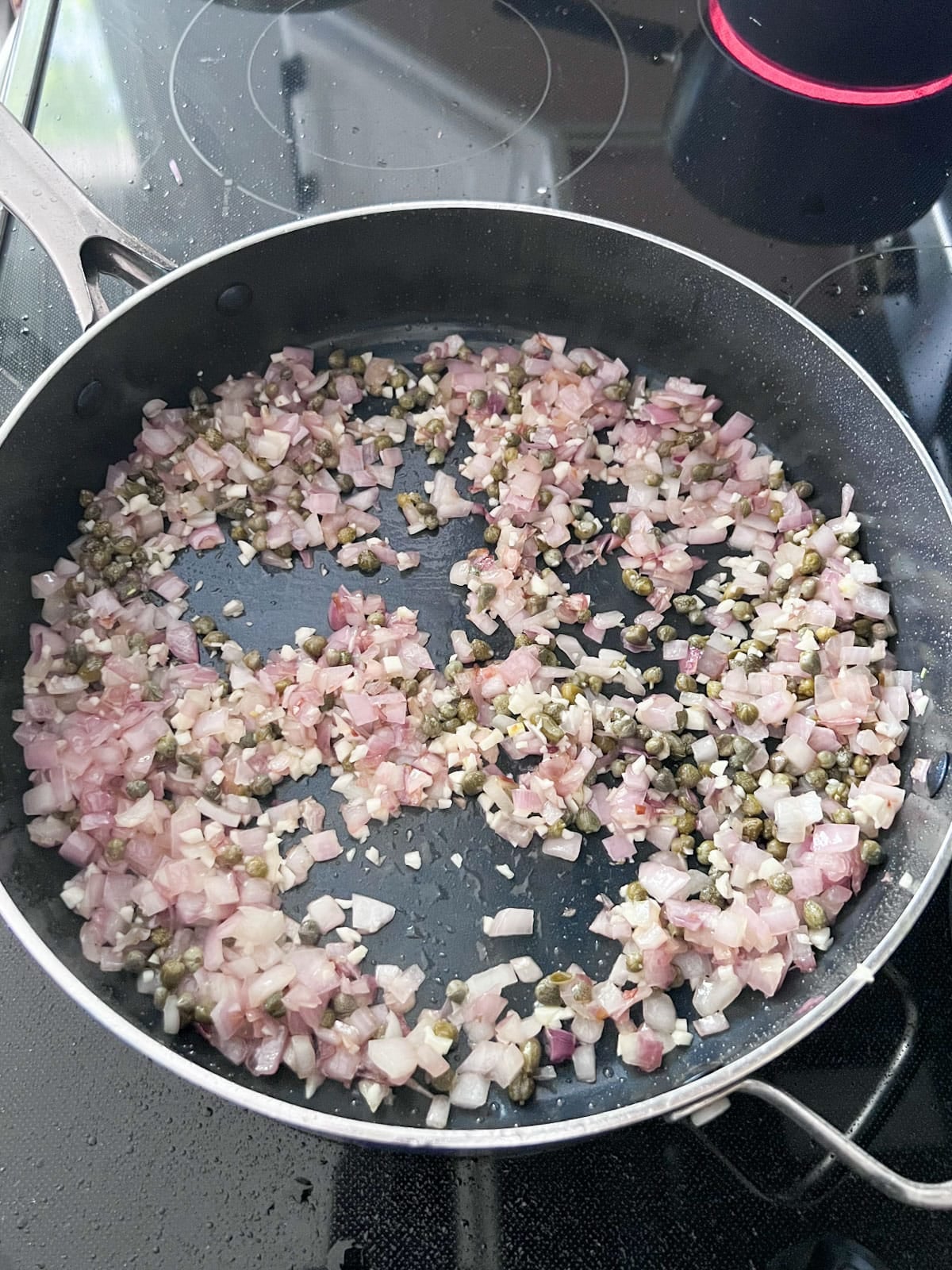 Onion, capers and minced garlic sautéing in a pan.