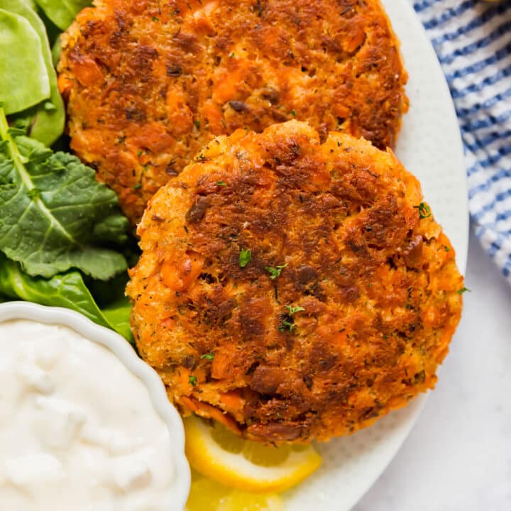 An overhead image of 2 salmon patties on a plate with mixed greens and tartar sauce.