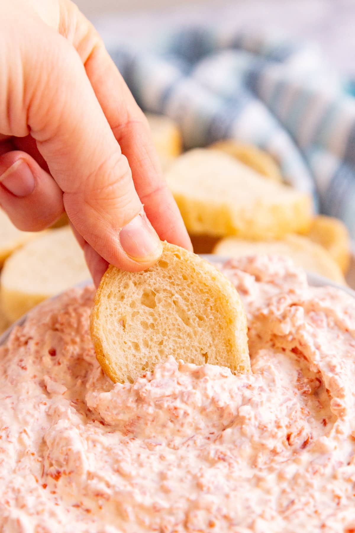 A hand dipping a slice of baguette into pepperoni dip.