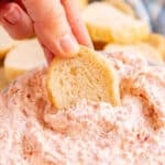 A hand dipping a slice of baguette into pepperoni dip.