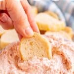 A hand dipping a slice of baguette into pepperoni dip.