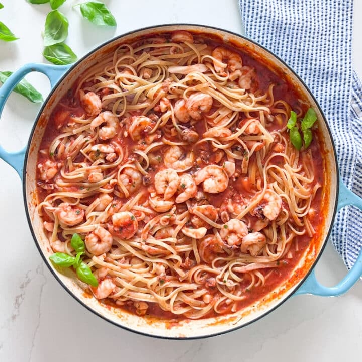 An overhead image of a pan of seafood fra diavalo with a striped napkin and fresh basil.
