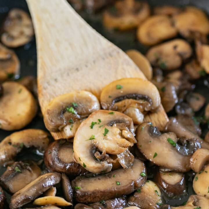 A wooden spoon in a pan of sauteed mushrooms.