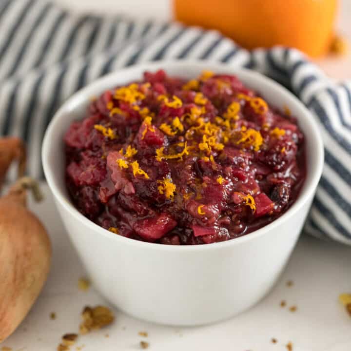 A white bowl of apple cranberry chutney with a striped napkin behind it.