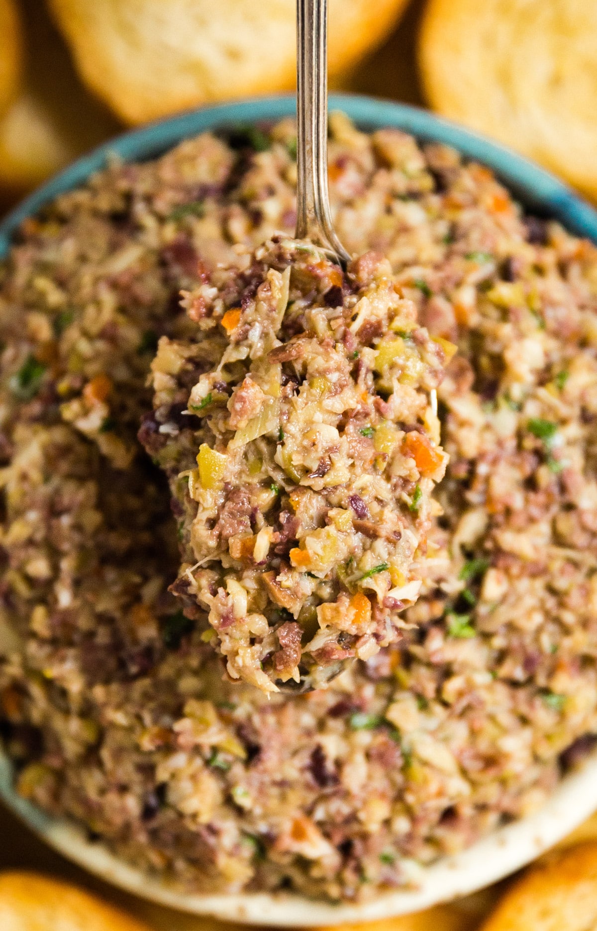 A spoon holding up a spoonful of olive tapenade from the bowl.