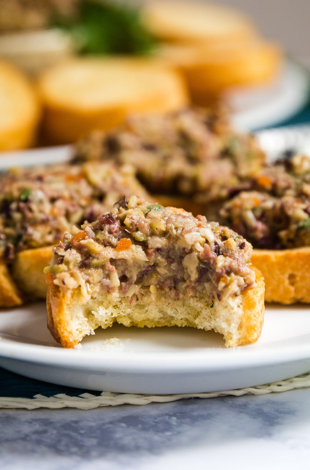 A close up of a baguette slice with olive spread on it and a bite taken out of it.
