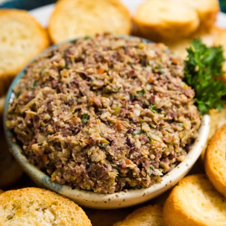 A bowl or artichoke and olive spread surrounded by toasted baguette.
