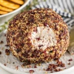 A cranberry cheeseball with a portion taken off it revealing the creamy interior.