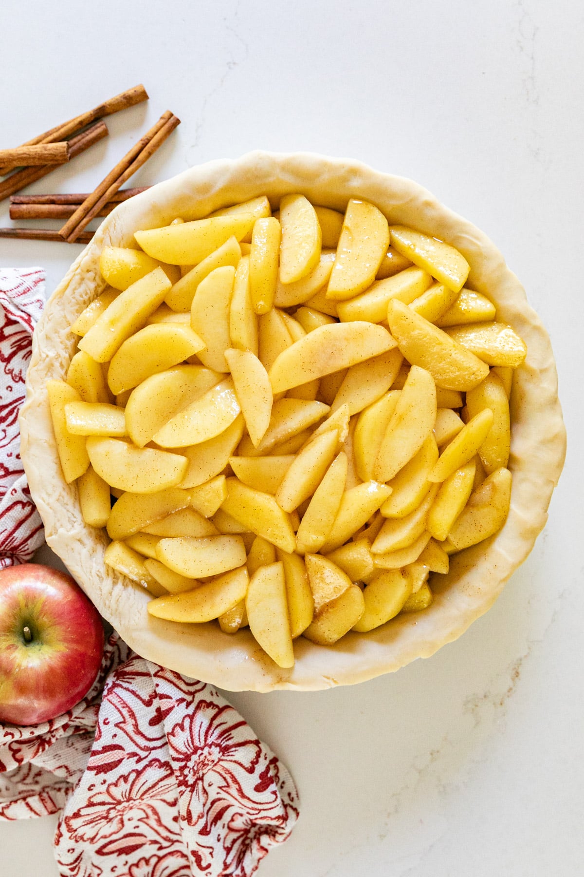 An overhead image of apple pie filling in a raw pie crust with apples and cinnamon sticks around it.