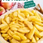 Apple pie filling in a raw pie crust with apples and cinnamon sticks behind it.