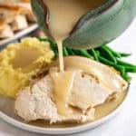 A green gravy boat pouring gravy onto a plate of turkey and mashed potatoes.