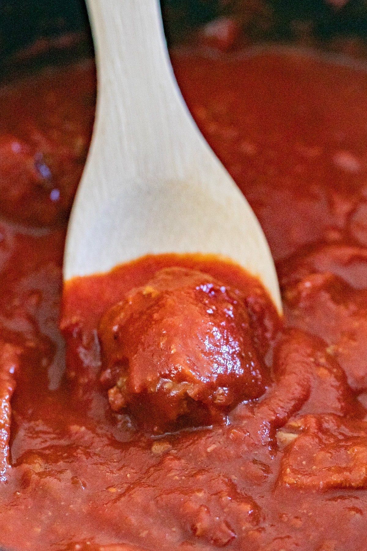 A wooden spoon scooping a meatball from a pot of sauce.