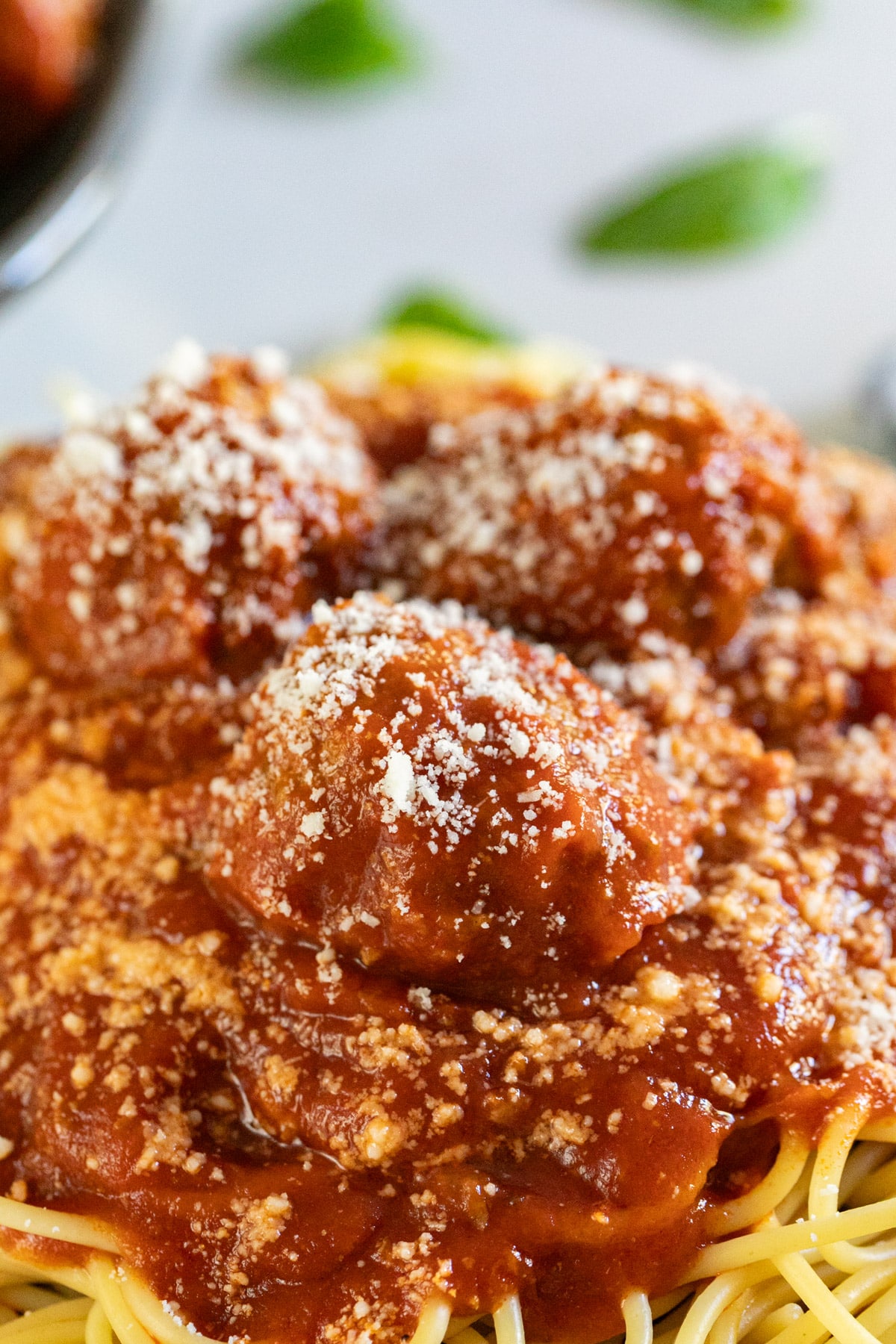 A meatball on a bed of pasta with sauce and Romano cheese sprinkled on top.