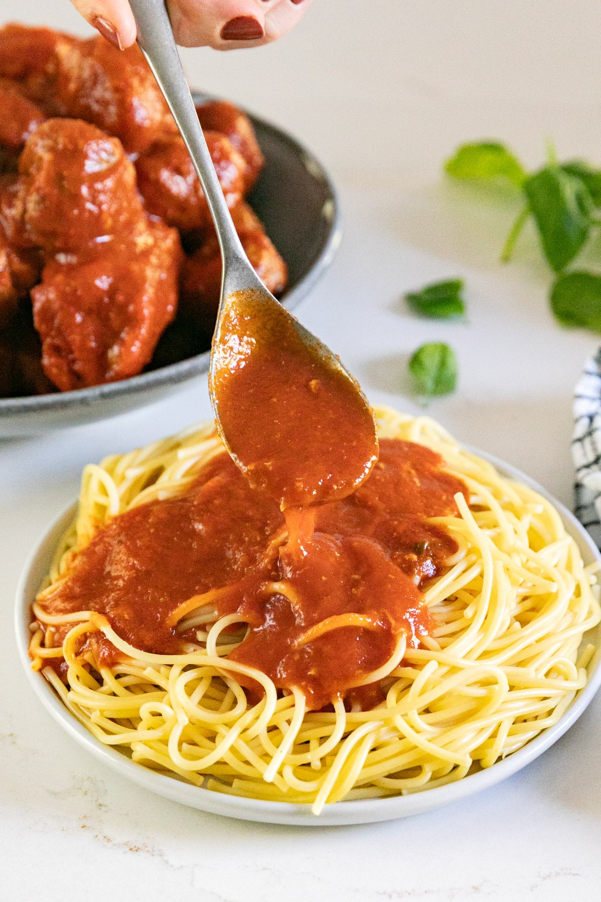 A spoon pouring this meat sauce recipe on a plate of spaghetti.