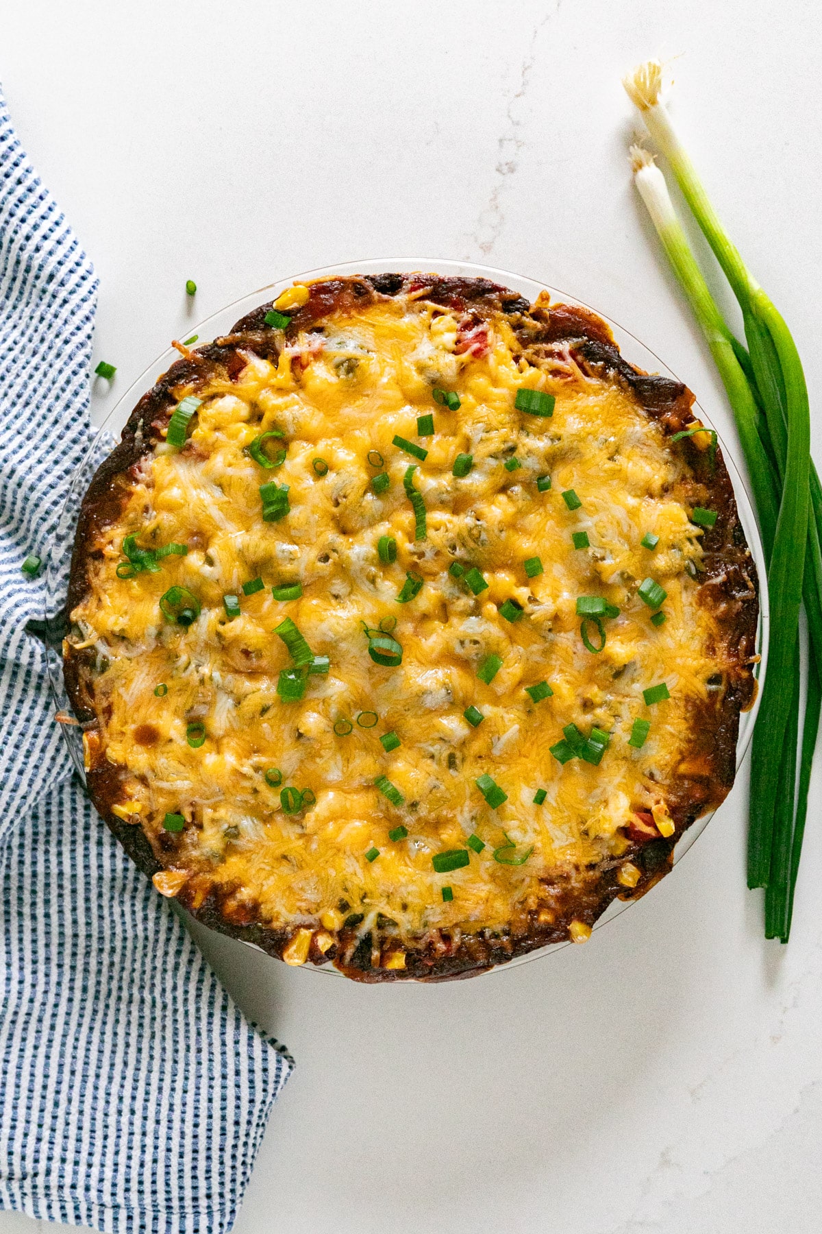 An overhead image of hot cheesy bean dip with a blue napkin and green onions on the side.