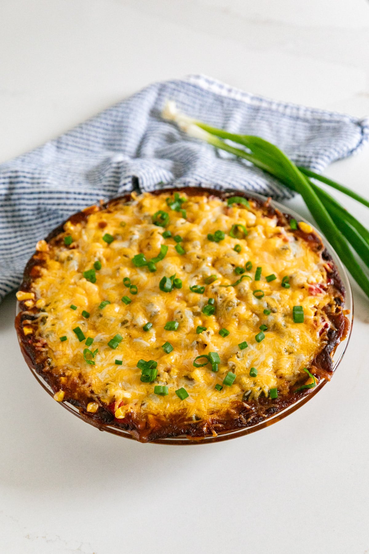 A pan of ben dip with a blue napkin and green onions in the background.