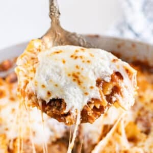 A spoon pulling up a scoop of skillet lasagna with melted cheese stretching behind it.