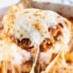 A spoon pulling up a scoop of skillet lasagna with melted cheese stretching behind it.
