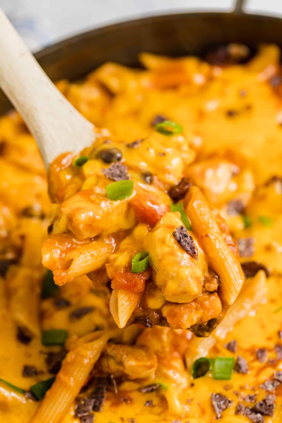 A wooden spoon holding up a scoop of taco pasta with chicken.