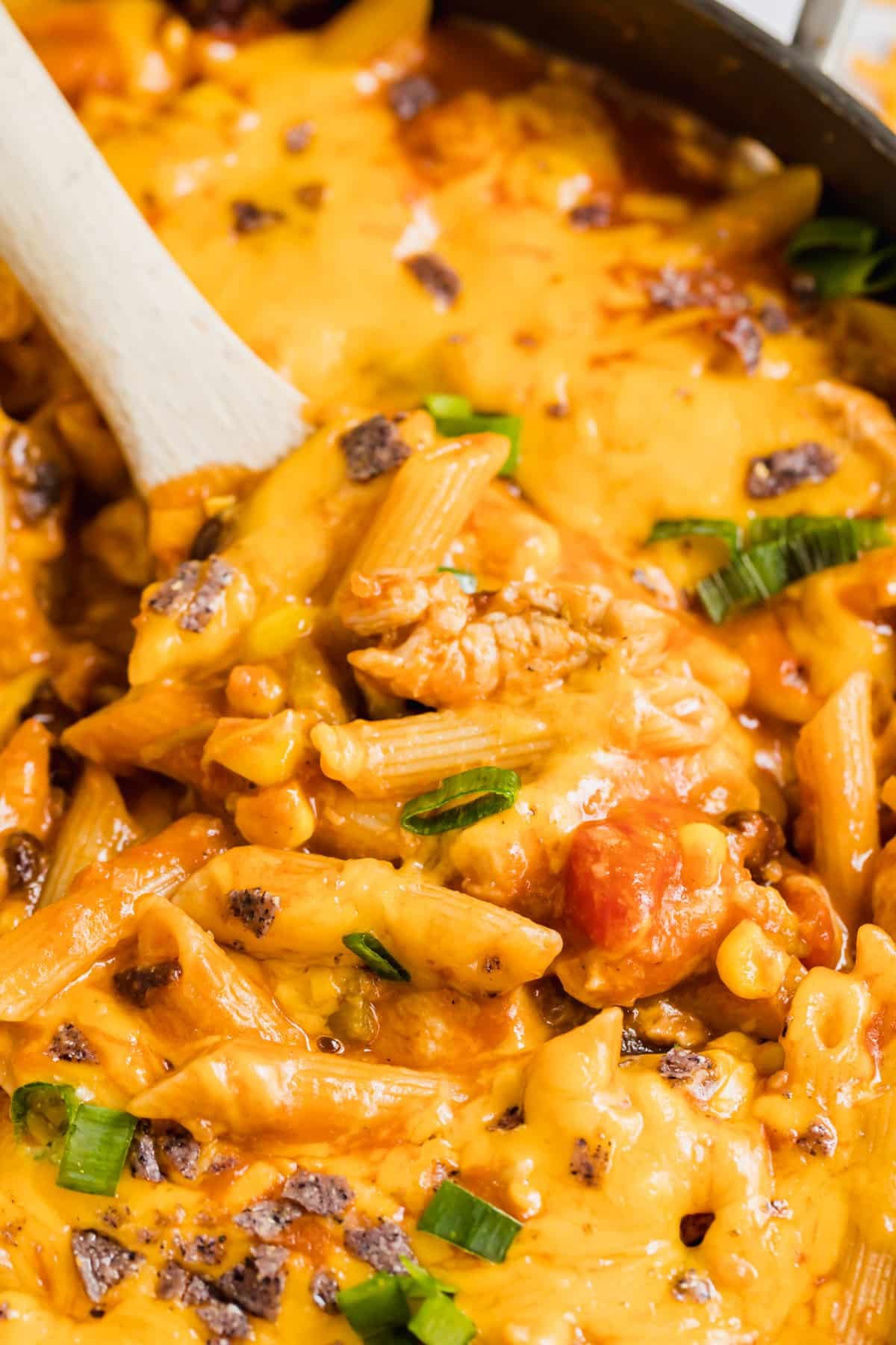 A close up of a wooden spoon in a pan of taco pasta.