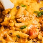 A close up of a wooden spoon in a pan of taco pasta.