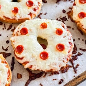 A close up of a bagel pizza with mini pepperonis on a pan.