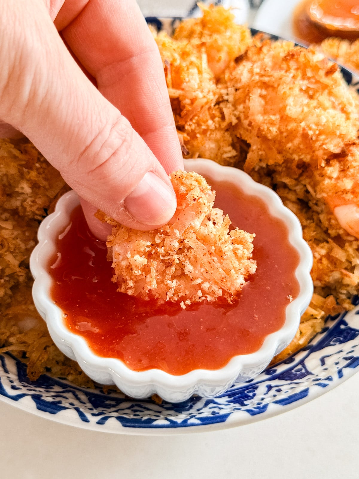 A hand dipping a coconut shrimp into the apricot dipping sauce.