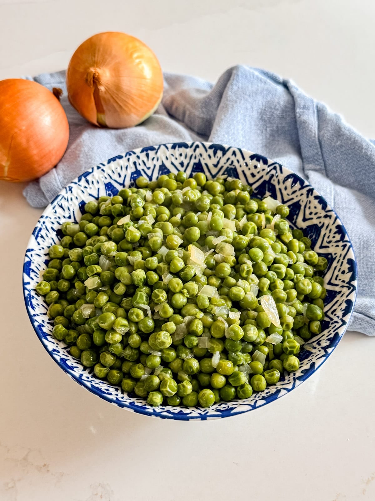 A bowl of peas with onions and a napkin in the background.
