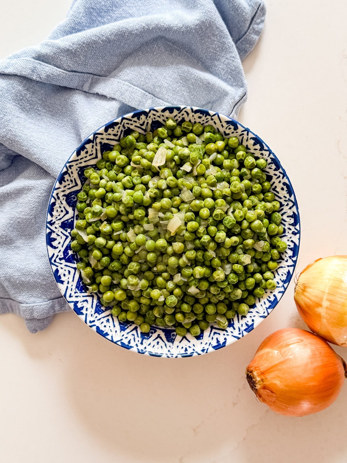 An overhead image of a bowl of green peas and onions.