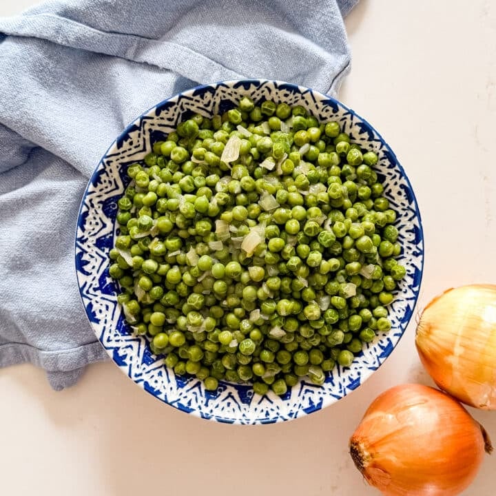An overhead image of a bowl of green peas and onions.
