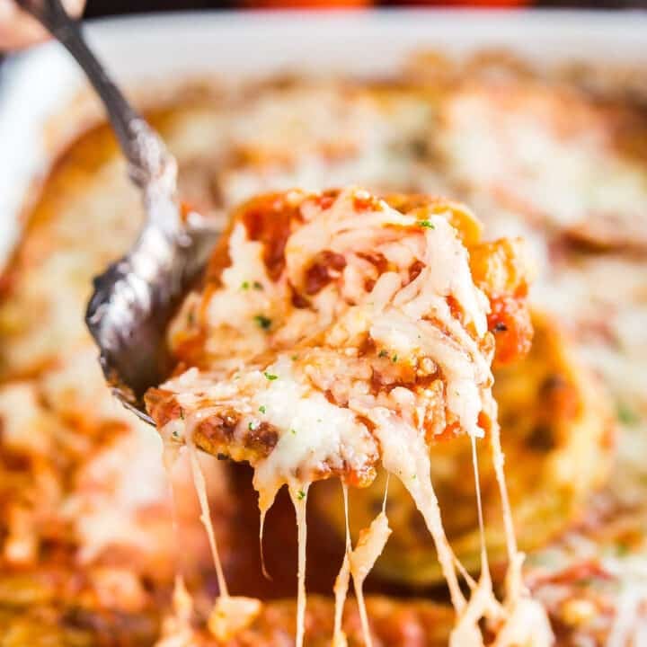 A spoon lifting up a scoop of eggplant parm bake with melt cheese trailing behind it.