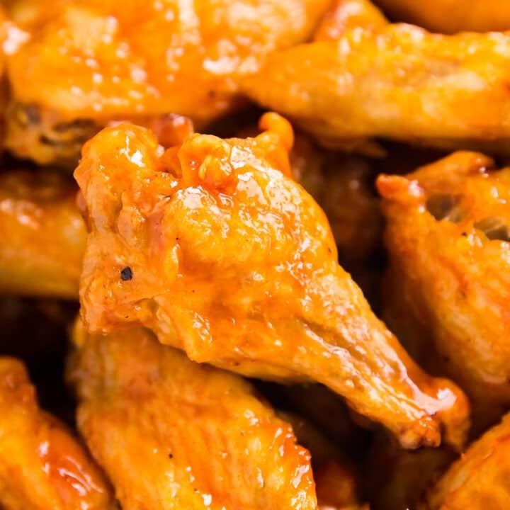 A close up of a drum chicken wing in a pile of other wings.