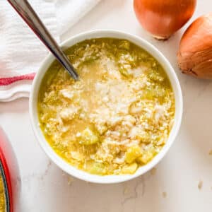 An overhead image of a bowl of zucchini soup with onions and a tea towel next to it.