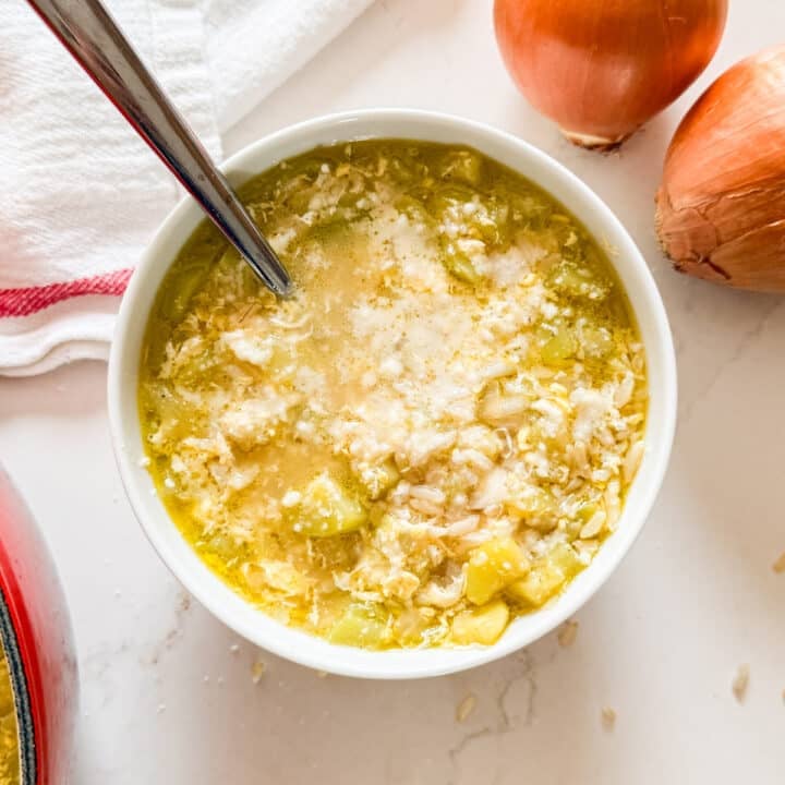 An overhead image of a bowl of zucchini soup with onions and a tea towel next to it.