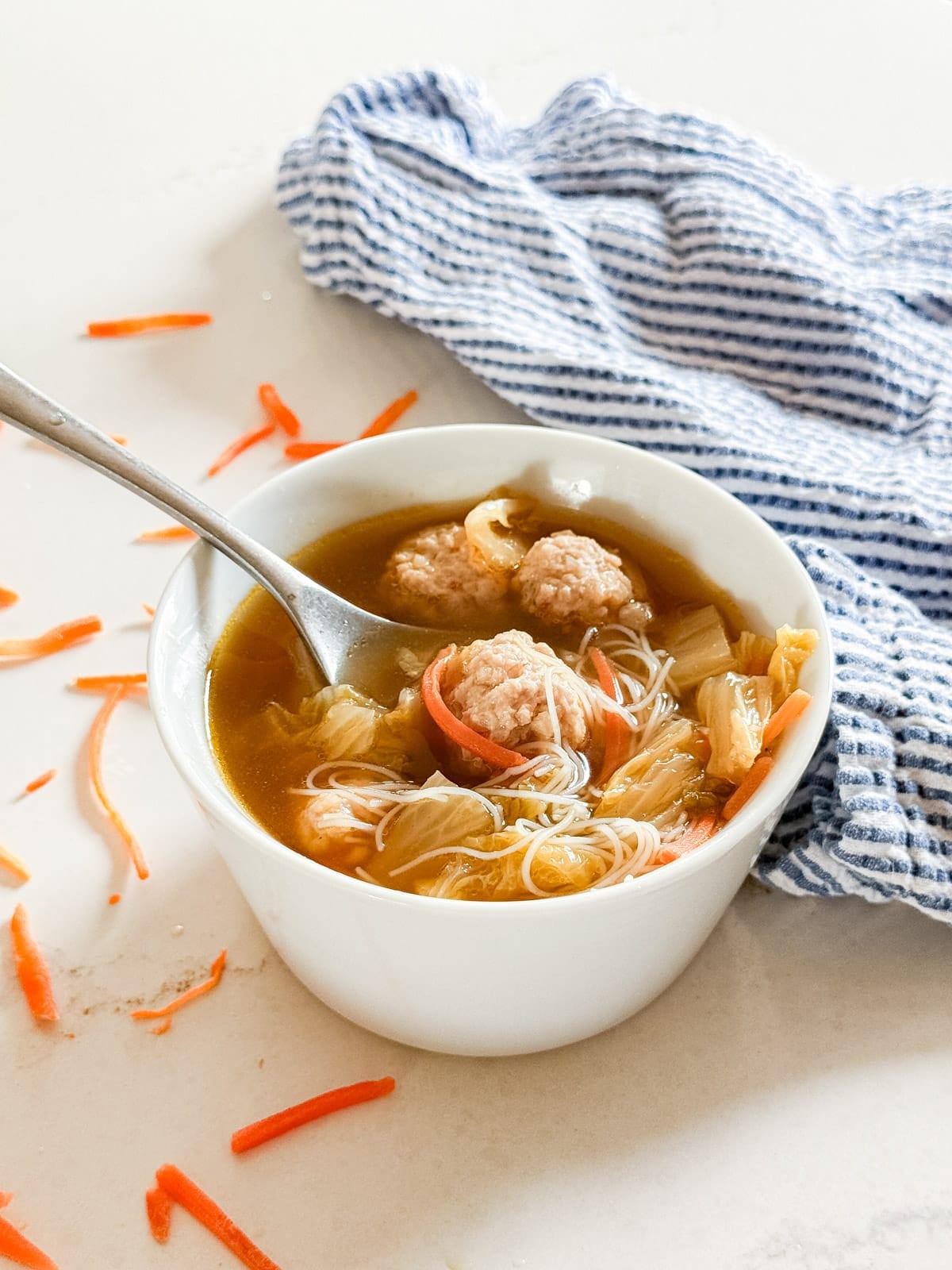 A bowl of asian soup with meatballs with a spoon and noodles in it.