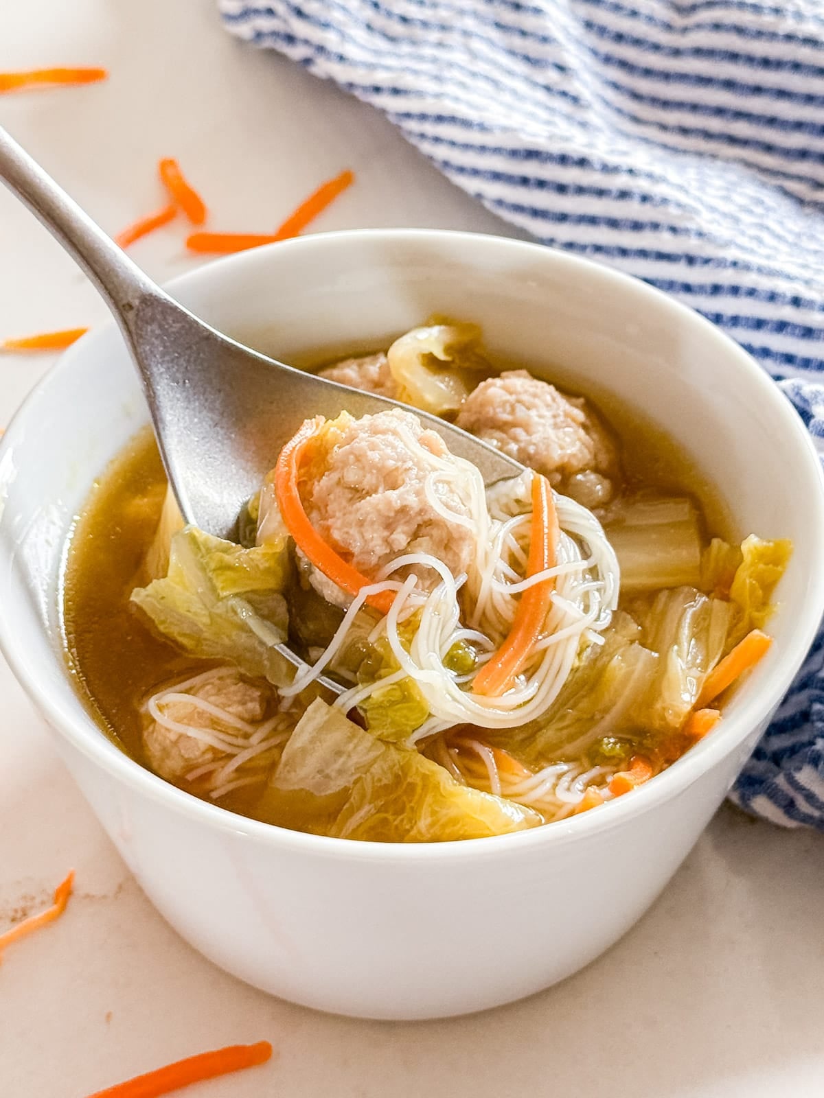 A close up of a spoon of soup and meatballs being lifted from the bowl.
