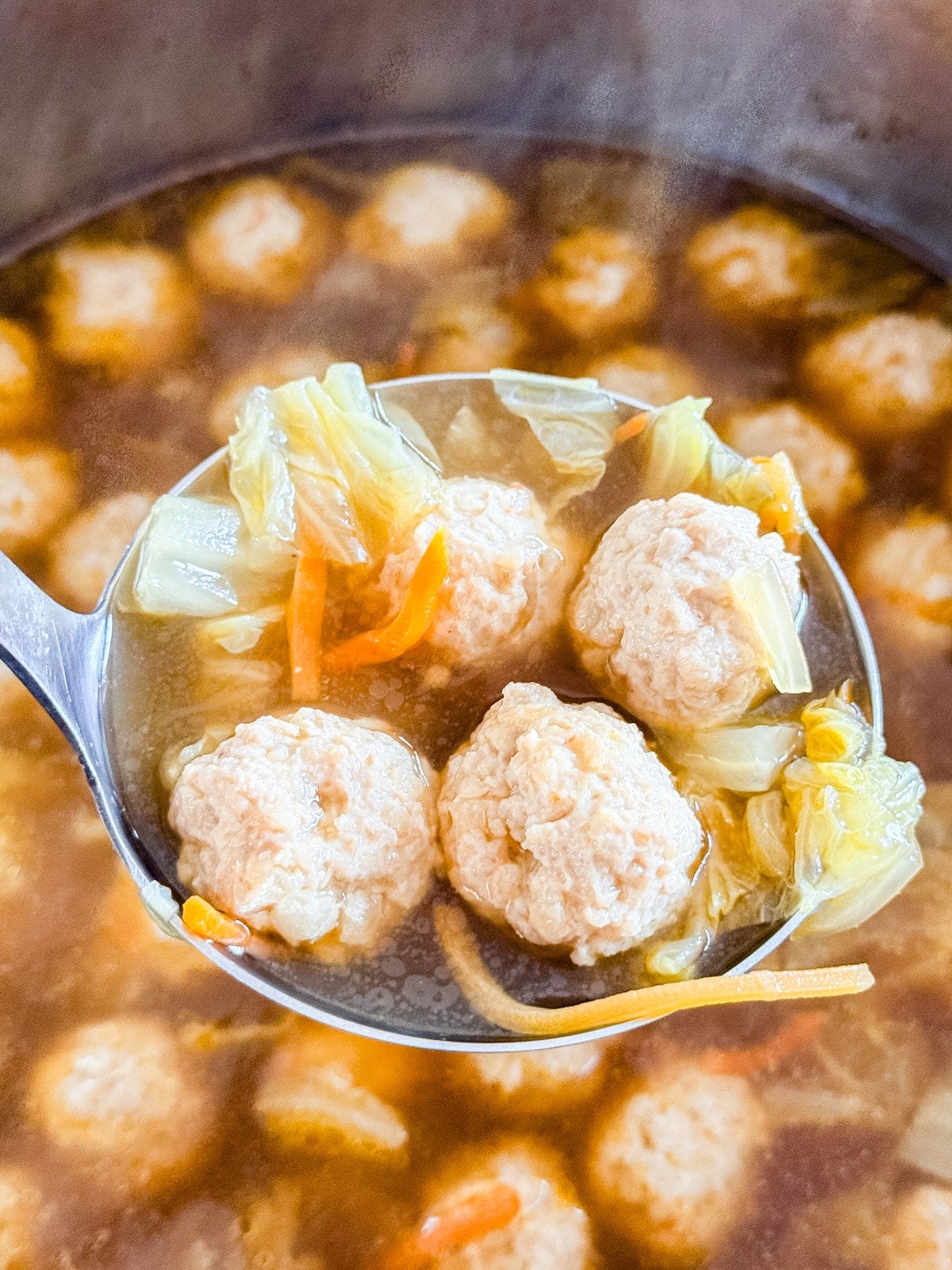 A ladle scooping Asian soup with meatballs and cabbage
