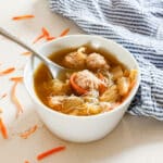 A bowl of asian soup with meatballs with a spoon and noodles in it.
