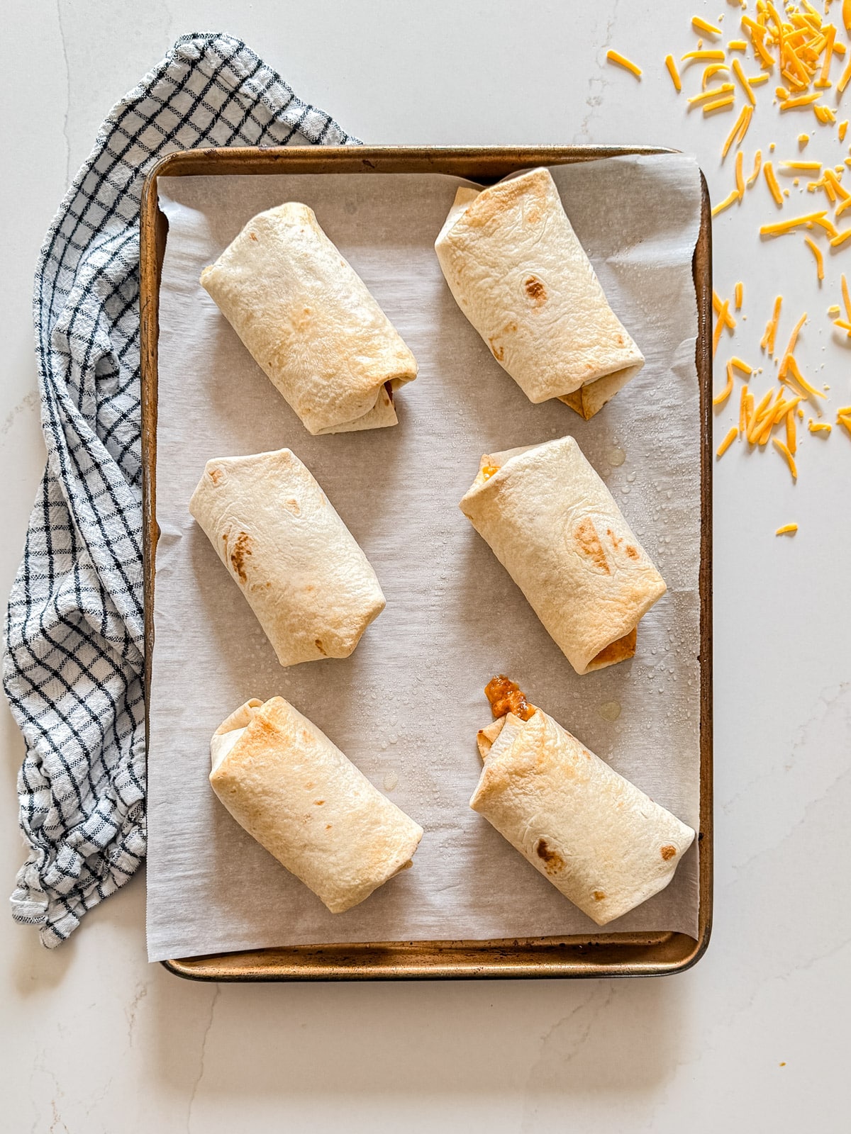 An overhead image of bean burritos on a sheet pan.