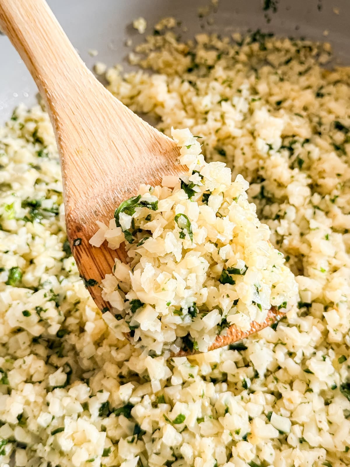A close up image of a wooden spoon holding a scoop of cilantro clime cauliflower rice.
